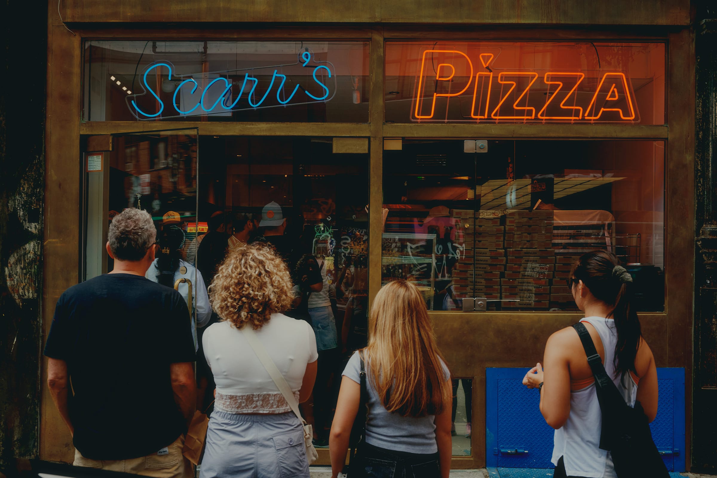 Four people stand outside waiting in line at the entrance of a pizza takeaway in Lower East Side, Manhattan.